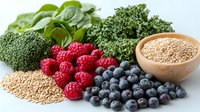 Fresh organic superfoods including blueberries, raspberries, kale, broccoli, quinoa and spinach leaves arranged on white background for healthy eating concept.