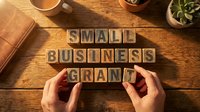 Small business grant wooden letter blocks on rustic desk with hands arranging text for entrepreneurship funding and startup support concepts.