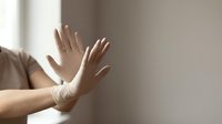 Hands pressed against frosted glass window creating dramatic silhouette effect with soft natural lighting and minimalist composition for emotional storytelling.