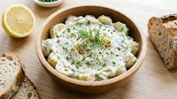 Creamy potato salad with fresh herbs and lemon in wooden bowl, served with sliced bread for lunch or dinner meal preparation.