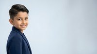 Young boy with dark hair and olive complexion wearing navy blue shirt, smiling at camera against white background. Suitable for educational materials, family websites, and children's content.