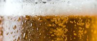 Closeup of golden beer with thick foam head and condensation droplets on glass, suitable for beverage advertising and hospitality design.
