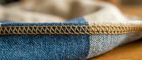 Close-up of denim fabric edge with decorative stitching and frayed hem detail. Textile craftsmanship showcasing blue jean material construction and seaming.