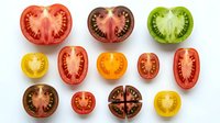 Sliced tomatoes in various colors and sizes arranged on white background, showing cross-sections of red, yellow, and green varieties for culinary, food styling, and recipe design use.