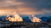 Industrial power plant with cooling towers emitting steam against dramatic sunset sky and snow-covered mountains in winter landscape for energy concepts.