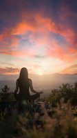 Woman meditating in lotus pose on mountain peak during dramatic sunset with orange and pink clouds creating peaceful spiritual atmosphere for wellness content.
