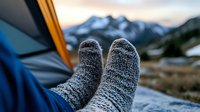 Cozy wool socks against mountain landscape background, feet resting in camping tent during sunset. Adventure lifestyle and outdoor relaxation concept.
