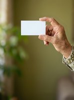 Mature man with tan skin holding blank white business card in hand against blurred green background, suitable for corporate branding and marketing materials.
