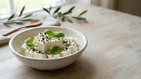 Fresh white cheese cubes with herbs and black sesame seeds in ceramic bowl on wooden table. Healthy Mediterranean appetizer ready to serve.