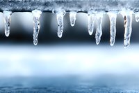 Frozen icicles hanging from roof edge against blurred winter background, crystalline formations catching light, creating natural winter atmosphere in cold weather.