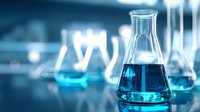 Laboratory glassware with blue liquid chemical solution in scientific research lab with blurred background of additional equipment.