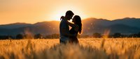 Romantic couple silhouette embracing in golden wheat field at sunset with mountain backdrop, warm lighting creates intimate mood for love concepts.