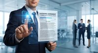 Professional businessman in suit touching digital licensing agreement interface in modern office environment with colleagues in background.