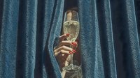 Mysterious person with red nail polish holding champagne flute behind blue velvet curtains for celebration and luxury lifestyle concepts.