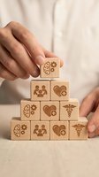 Hands building pyramid with wooden blocks featuring healthcare symbols including brain, heart, medical cross and caduceus representing wellness strategy.