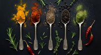 Colorful spices and herbs arranged on vintage spoons with fresh rosemary and chili peppers on dark slate background for culinary cooking and seasoning.
