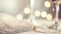 Elegant white ceramic bowl with golden pearls and lace on soft fabric surface with warm bokeh lights creating luxurious spa atmosphere for relaxation.
