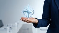 Business professional holding glowing compass rose symbol in open palm representing navigation, direction, guidance and strategic planning in corporate environment.