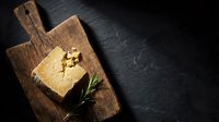 Overhead view of melted butter on wooden cutting board with fresh rosemary sprig on dark slate surface, ideal for culinary and food styling projects.