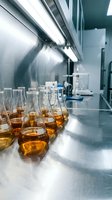 Laboratory glassware with amber liquid samples on steel counter under ventilation hood for scientific research and chemical analysis experiments.