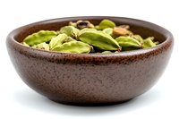 Green cardamom pods in brown ceramic bowl on white background, aromatic whole spice used in Indian cuisine and baking, close up macro shot.