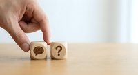 Hand placing wooden cube with question mark next to cube with keyhole symbol on desk representing problem solving and finding solutions in business.