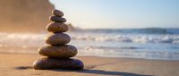 Balanced stone cairn on sandy beach with ocean waves and golden sunset light creating peaceful zen meditation atmosphere for wellness and mindfulness practices.