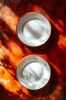 Empty white porcelain plates with gold trim on vibrant orange background with dramatic shadow play and light effects creating artistic composition.