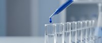 Laboratory pipette dropping blue liquid into test tubes for scientific research and chemical analysis in modern lab setting.