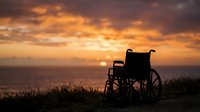 Silhouette of empty wheelchair against dramatic golden sunset sky over ocean horizon, symbolizing hope, recovery, and resilience for healthcare and wellness campaigns.