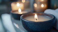 Burning candle in dark blue ceramic holder creates warm ambient lighting with soft bokeh background for relaxation and home decor atmosphere.