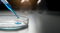 Laboratory pipette dropping blue liquid sample into petri dish for scientific research and medical testing analysis in modern lab setting.