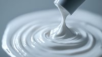 Smooth flowing white liquid creating concentric ripples and swirls against gray background, close-up macro photography showing creamy texture and glossy surface finish.