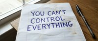 Handwritten motivational quote on lined paper saying you can't control everything with pen on wooden desk for mindfulness and stress management concepts.