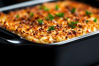 Creamy potato gratin with golden brown crust topped with fresh herbs in black baking dish, macro food photography with selective focus and rich texture.