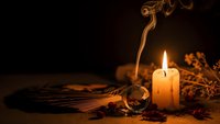 Mystical fortune telling scene with burning candle, tarot cards, crystal ball and incense smoke creating atmospheric divination setting for spiritual readings.