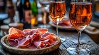 Two glasses of sparkling rosé wine with charcuterie meat platter on rustic wooden table for romantic dinner celebration and gourmet food pairing experience.