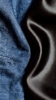 Blue denim fabric with detailed stitching contrasts against smooth brown leather material creating textural fashion background for clothing design projects.