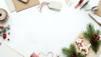 Flat lay workspace with evergreen branches, festive ornaments, kraft envelope, twine, and stationery arranged on white background for holiday greeting card design.