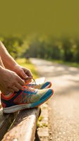 Senior runner tying colorful athletic shoes on wooden bench before morning jog on sunny park path for fitness and healthy lifestyle motivation.