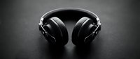 Black over-ear headphones with metal headband on dark textured surface, isolated for audio equipment, music production, and technology design projects.