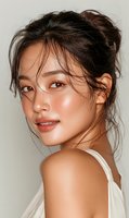 Young Asian woman with glowing skin and messy bun hairstyle looking over shoulder with natural makeup and dewy complexion for beauty and skincare concepts.