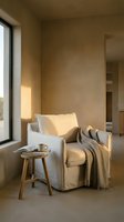 Minimalist reading nook with neutral upholstered armchair, wooden side table, warm blanket, and natural light from large window in calm beige interior space.