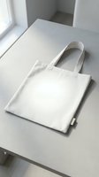 Blank white canvas tote bag with handles displayed on neutral surface, ready for custom branding, printing, or design projects for retail and promotional use.