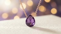 Faceted amethyst gemstone pendant hanging from delicate chain on white surface with warm bokeh lights in background, suitable for jewelry marketing and luxury product promotion.