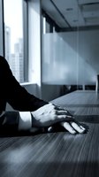 Businessman hands clasped on conference table in modern office, blue toned monochrome atmosphere conveying focus, authority, and corporate professionalism.
