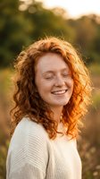 Happy young Caucasian woman with curly red hair and freckles smiling with eyes closed in warm golden hour sunlight outdoors in natural setting.