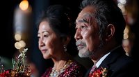 Elegant senior Asian couple in formal evening wear at upscale event with warm bokeh lighting creating romantic atmosphere for luxury lifestyle content.