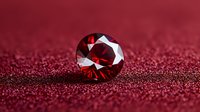 Round cut ruby gemstone on sparkling red glitter background, macro photography showing brilliant facets and luxury jewelry details in dramatic lighting.