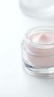 Open glass jar containing pale pink cosmetic cream or moisturizer on white background, isolated and ready for skincare, beauty product, and cosmetics design use.